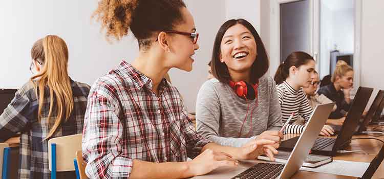 two students laughing while working together on laptops