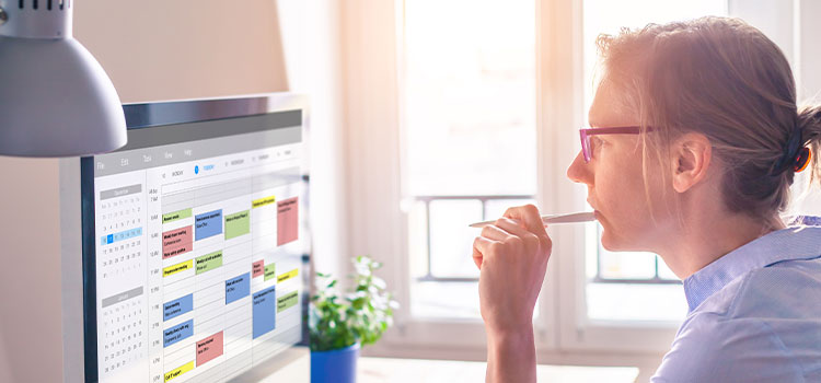 a woman at a desk works on a schedule on her laptop