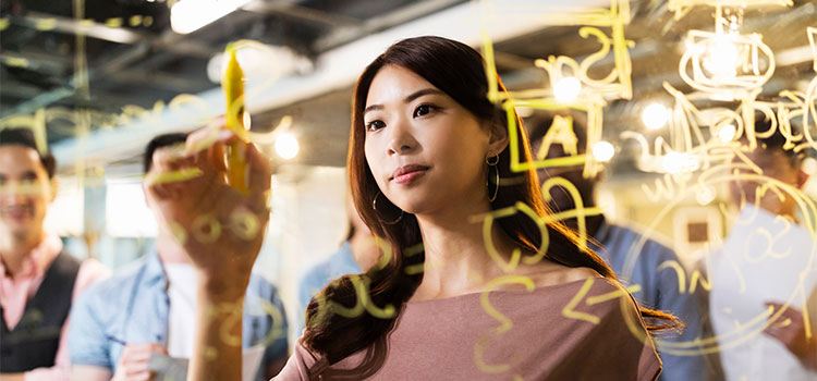 a woman works on an equation on a glass board as others look on