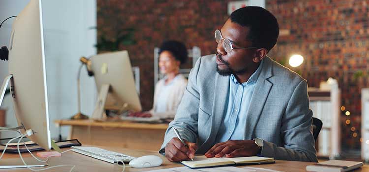 business administrator takes notes of data from desktop monitor