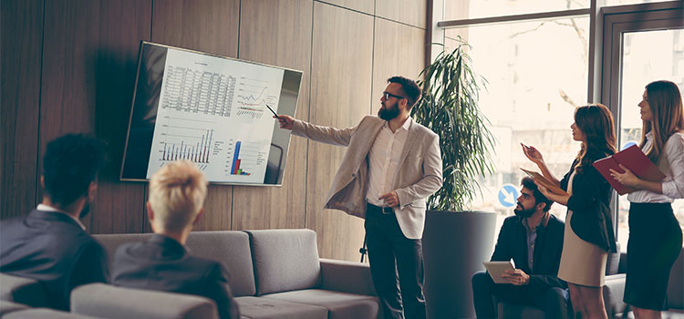 a man explains charts and numbers on a screen to other professionals