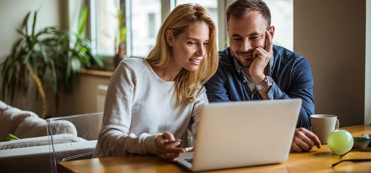 a man and a woman talk as they read information on a laptop 