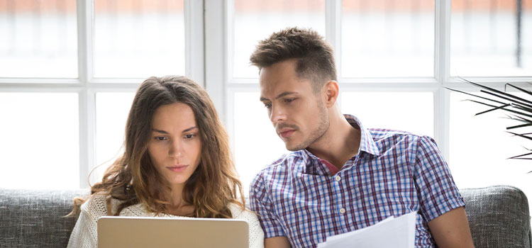 A man and a  woman sit on a couch as they look at information online
