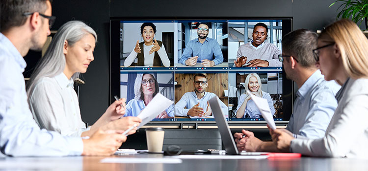 Four professionals at a table talk on a video conference call with colleagues