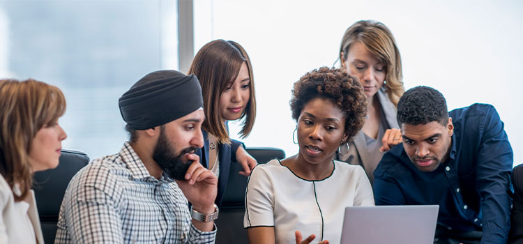 Staffers gather around a woman as she explains something on her laptopeather