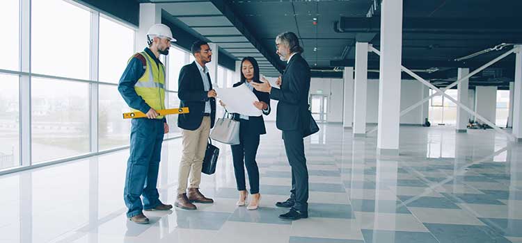 A group of business professionals review a building plan with an architect in a commercial office building.