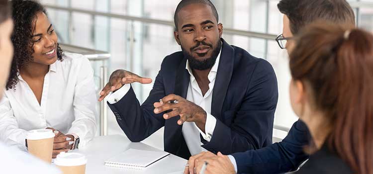 four people at desk listening to man talking