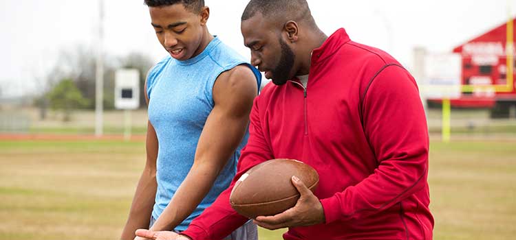 male coach showing football player how to hold ball