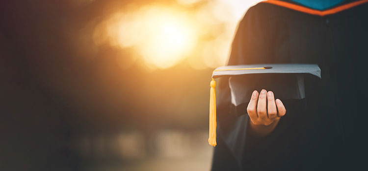 cropped image of graduate level student in cap and gown with sun shining behind