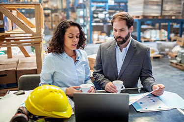 a man and a woman in a warehouse review information on a laptop