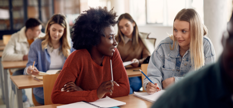 two diverse college students seated and talking in a classroom